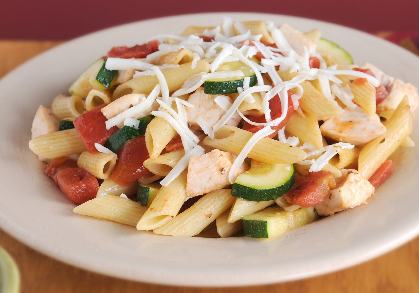 Penne pasta with zucchini, tomatoes, and chicken, topped with shredded cheese
